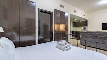 A hotel room with a bed, a wardrobe, a kitchenette, and a seating area.
