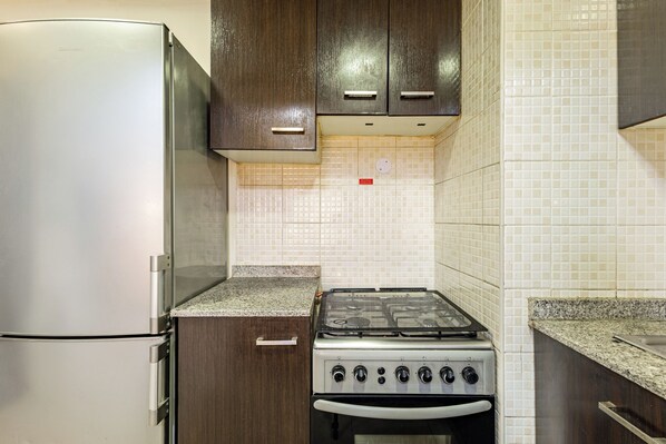 A compact kitchen with a refrigerator, stove, and cabinets. - Studio Retreat In Reemram Pool & Gym (Dubai)