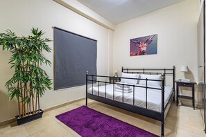 A bedroom with a bed, a window with a blind, a painting, a plant, and a purple rug. - Studio Retreat In Reemram  Pool & Gym (Dubai)