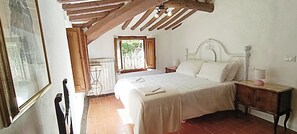 Une chambre à coucher avec un grand lit, une tête de lit en bois, une table de chevet et une fenêtre donnant sur un paysage verdoyant.