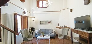 Un salon comprenant un canapé, deux fauteuils, une table basse, un téléviseur et un escalier.