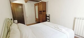 A bedroom with a bed, a wooden wardrobe, a mirror, and a radiator. - Melchiade Uno Colonial House, a country cottage in the hills for 8 people, near Lucca (Borgo a Mozzano)