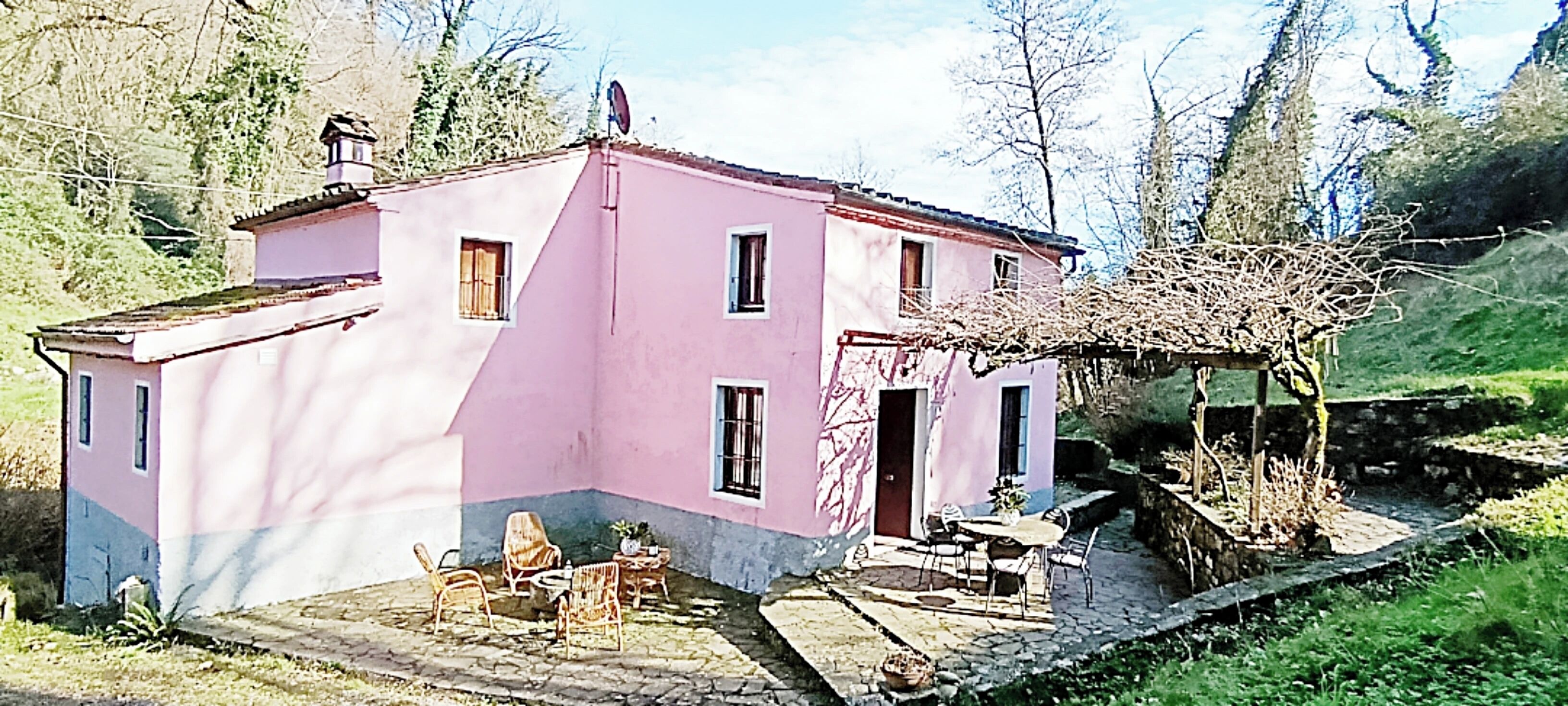 Ein rosafarbenes Haus mit Garten, einer Terrasse mit Stühlen und einem kleinen Tisch.