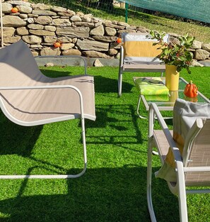 Een terras met twee loungestoelen en een kleine tafel, omringd door kunstgras en een stenen muur.