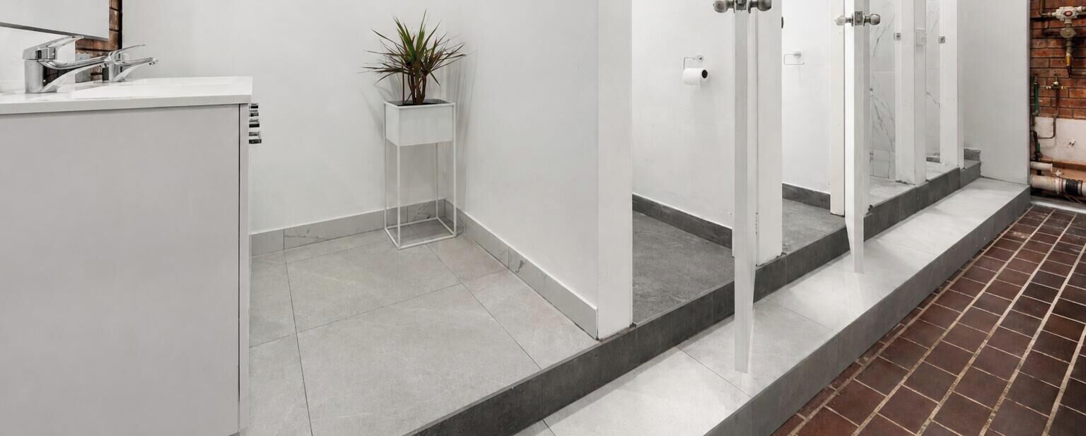 A modern bathroom with a white sink, a potted plant, and a tiled floor.