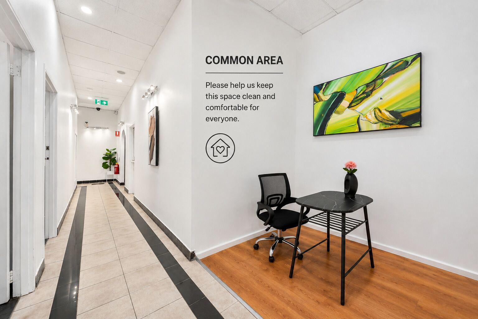 A hallway with a common area sign, a painting, a chair, and a table.
