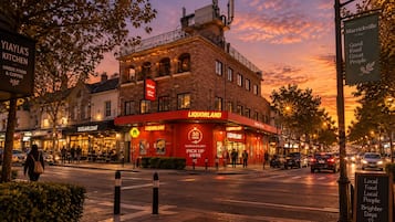 A street view at dusk with a prominent Liquorland bar and adjacent Greek food and coffee shop.