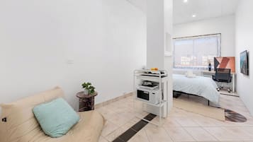 A modern bedroom with a bed, a desk, and a small kitchenette.