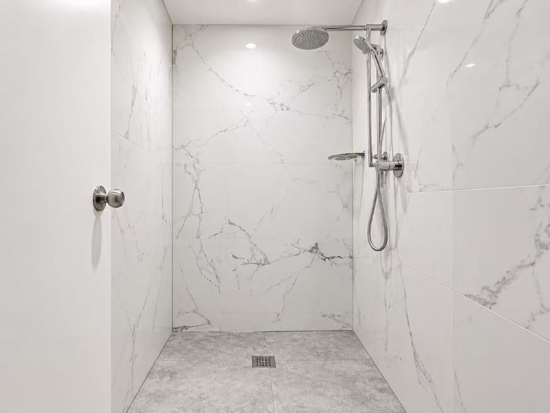 A modern bathroom with a shower, marble walls, and a visible drain.