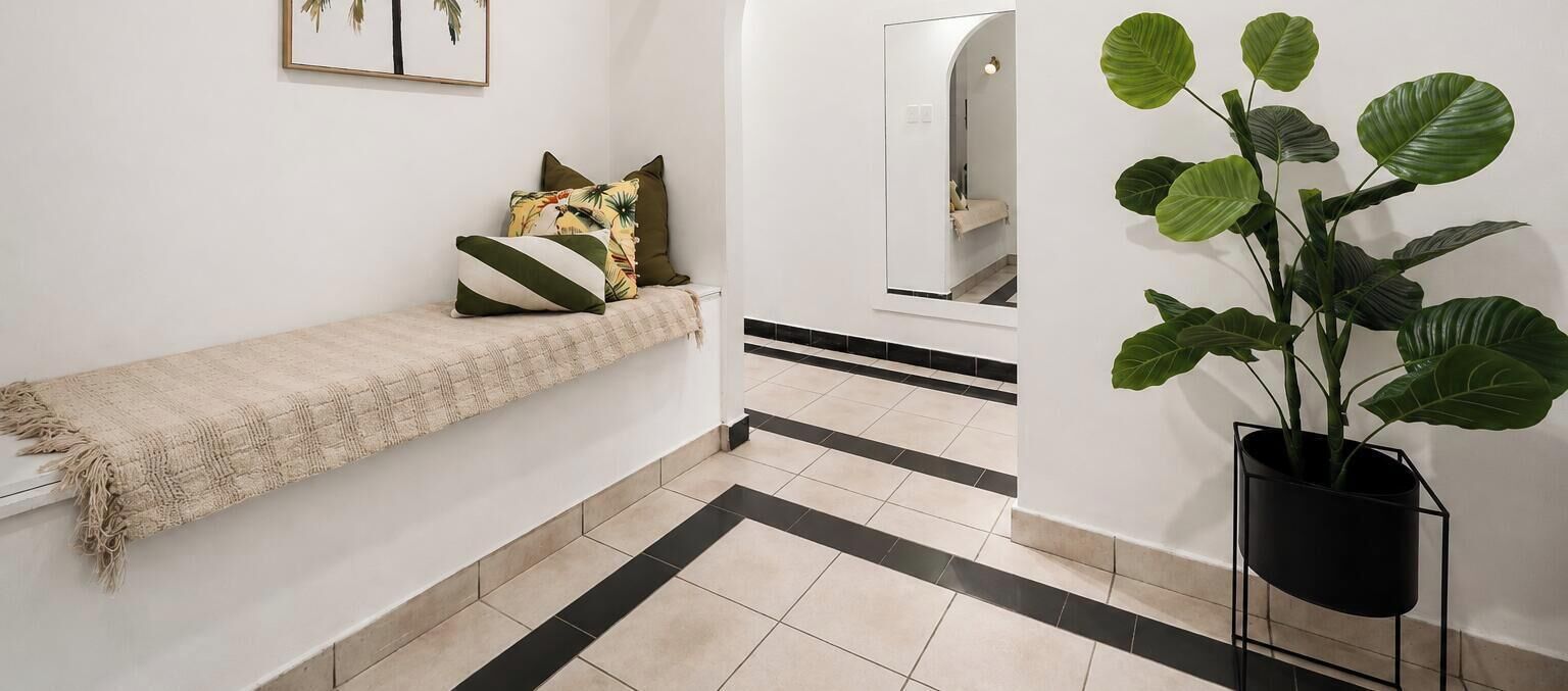 A hallway with a bench, a potted plant, and a mirror on the wall.