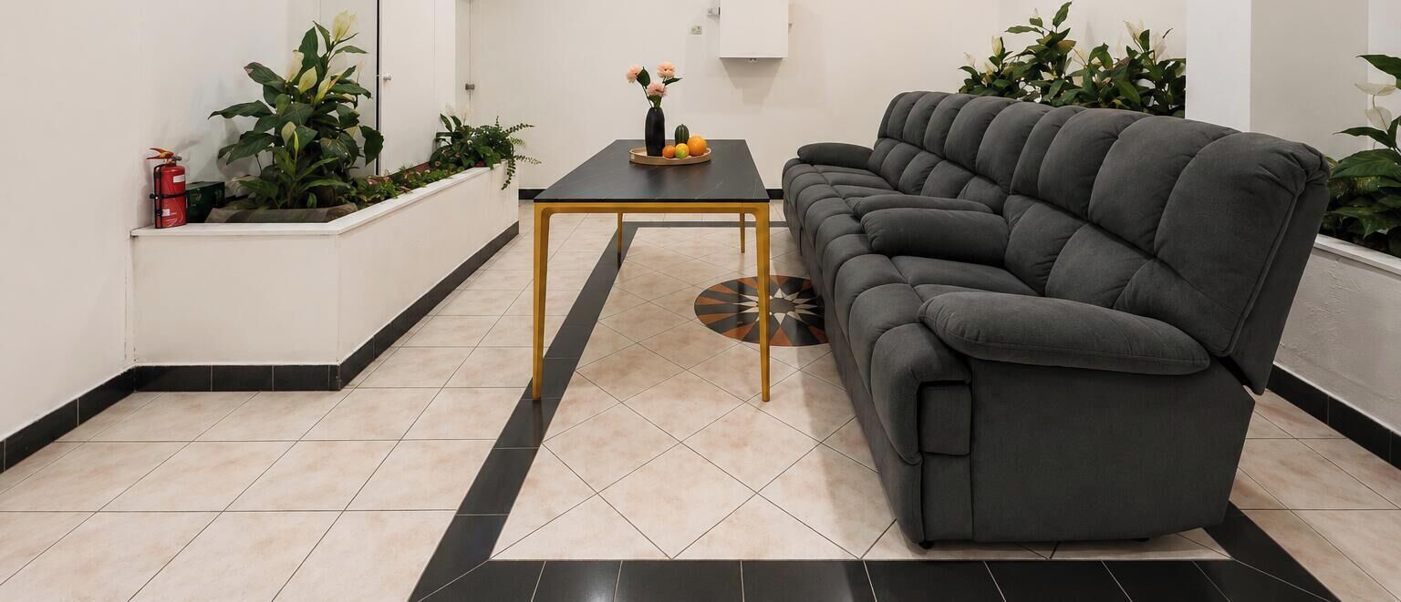 A modern living room with a dark grey sofa, a small black coffee table, and a tiled floor with a black border.