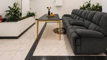 A modern living room with a dark grey sofa, a small black coffee table, and a tiled floor with a black border.