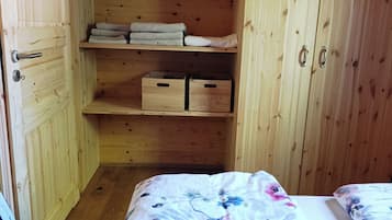 Ein Zimmer mit Holzboden, einem Bett, einem Regal mit gefalteten Handtüchern und einem Holzkasten.