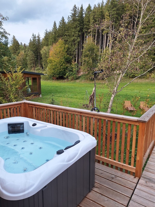 A hot tub on a wooden deck with a view of a grassy yard and trees.