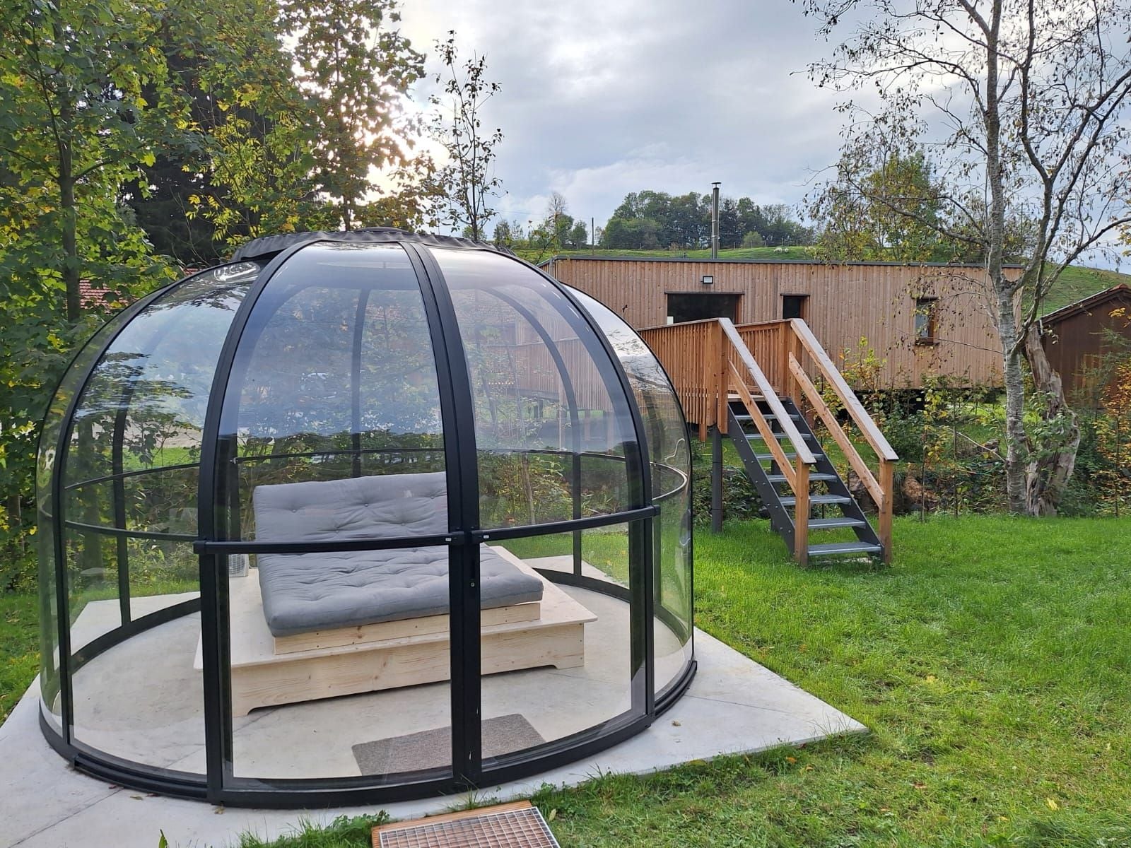 A circular glass-enclosed structure with a cushioned seating area and a wooden platform.