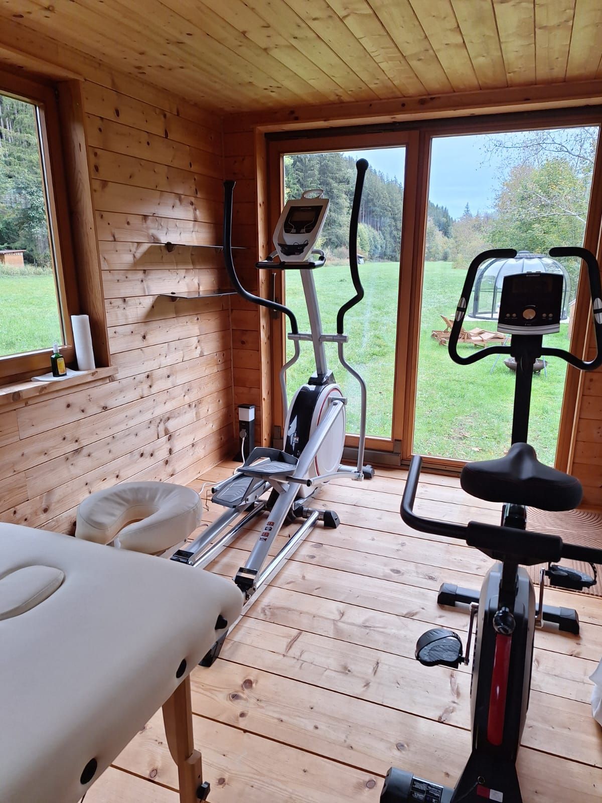 A wooden room with a stationary bike, a rowing machine, and a massage table.