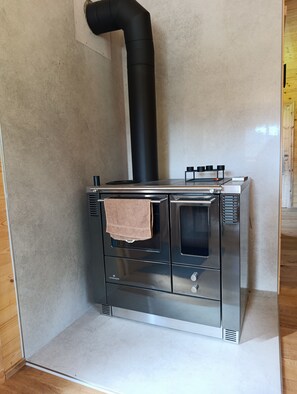 A stainless steel stove with a black chimney, a towel hanging on the door, and a small shelf with items on top.