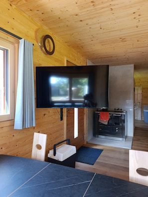 A wooden interior with a flat-screen TV mounted on the wall, a kitchen area with a microwave, and a dining space with a table and chairs.