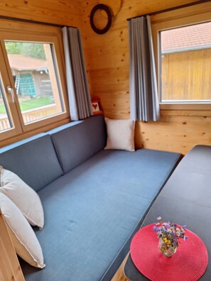 A room with a sofa, a small table with a vase of flowers, and a window with curtains.