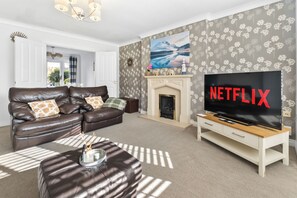 A modern living room with a leather sofa, a fireplace, a television, and a floral wallpaper. - Spacious 5 Bed 2 Bath House • Driveway Parking • Near NEC • Solihull • Airport (Balsall Common)
