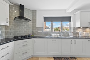 A modern kitchen with white cabinets, a black stove, and a window with a view of the outside. - Spacious 5 Bed 2 Bath House • Driveway Parking • Near NEC • Solihull • Airport (Balsall Common)