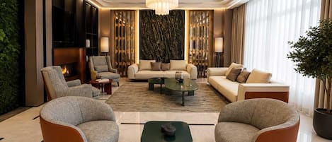 A modern living room with a fireplace, comfortable seating, and a decorative chandelier.