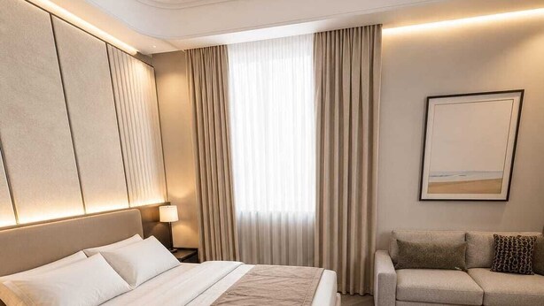 Habitación de hotel con una cama grande, un sofá, una mesita de noche, una lámpara y un cuadro en la pared.