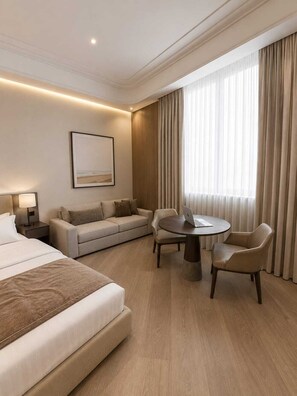 A hotel room with a bed, a sofa, a desk with a laptop, and a dining table with chairs.