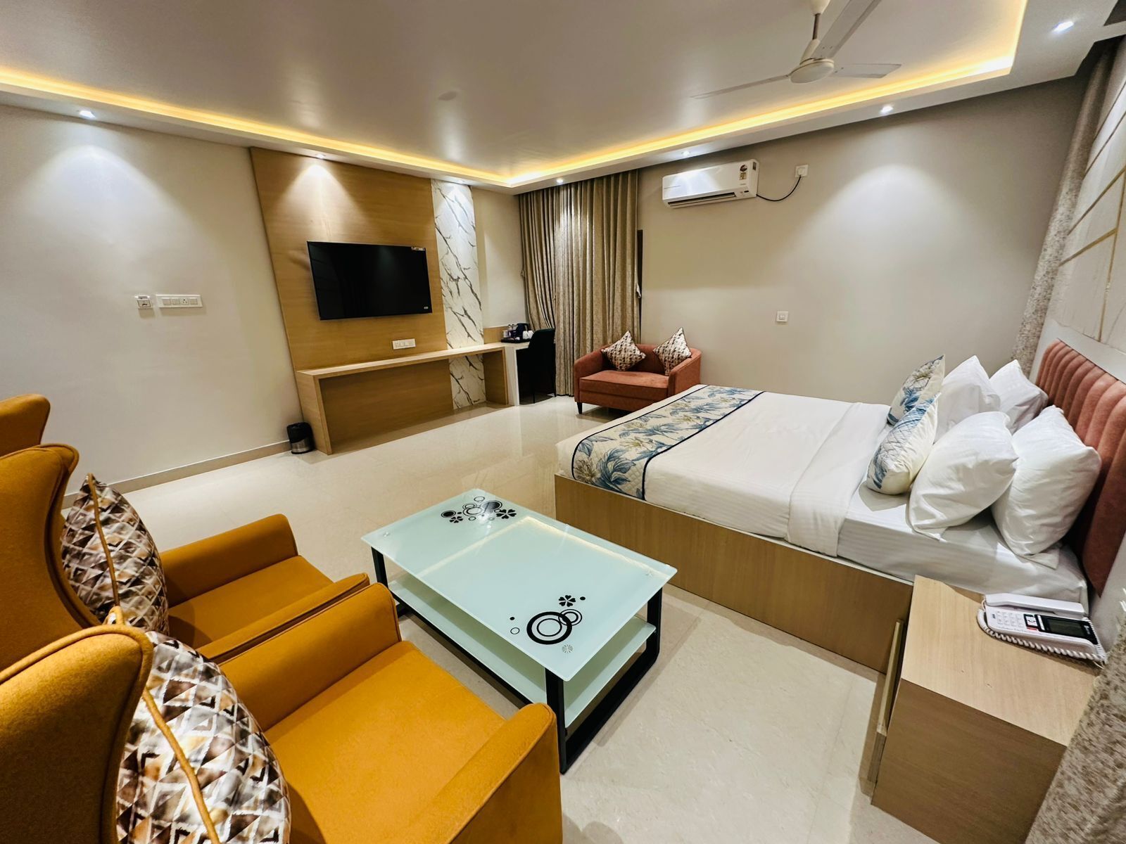 A hotel room with a bed, a sofa, a small table, a TV, and an air conditioning unit.