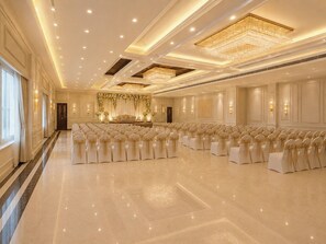 A spacious hall with rows of chairs, a stage with a floral backdrop, and elegant chandeliers. - HOTEL ADITYA MARINE GARDEN (Patna)