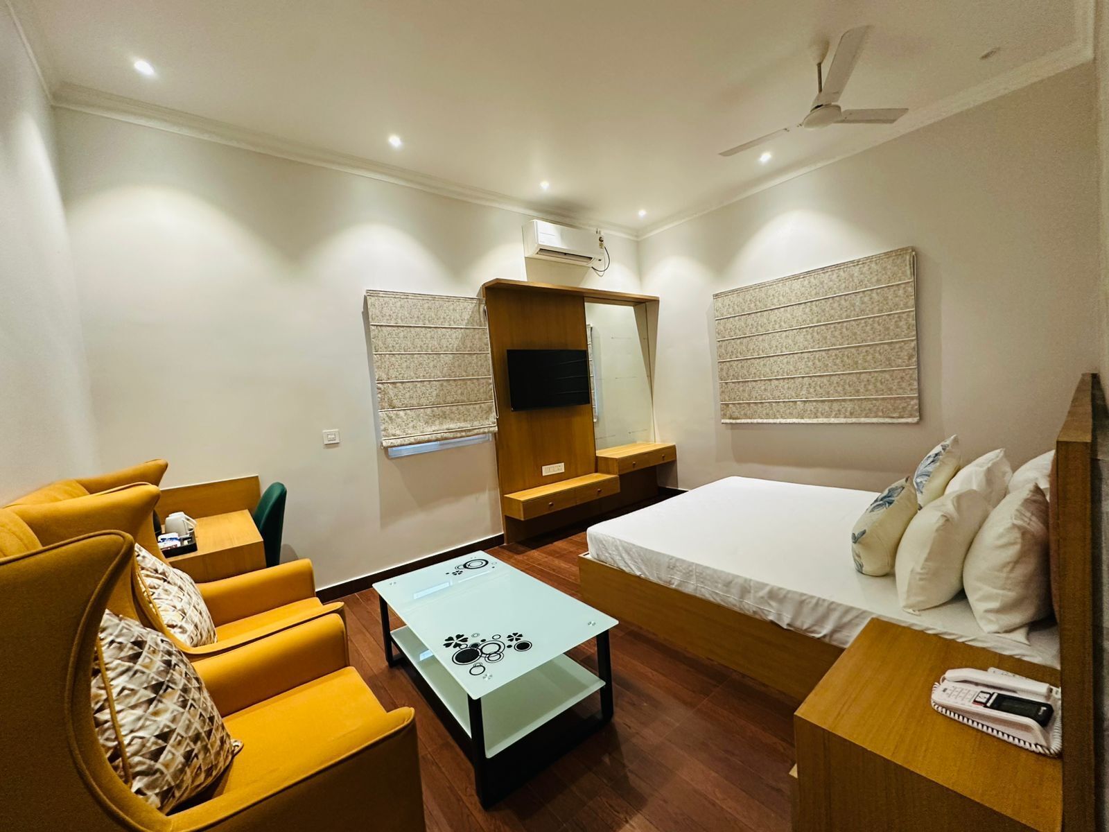 A compact hotel room with a bed, a sofa, a small table, a mirror, and a TV.