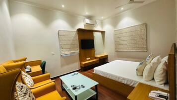 A compact hotel room with a bed, a sofa, a small table, a mirror, and a TV.