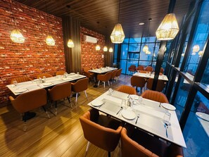 A restaurant with brick walls, wooden floors, and orange chairs. Tables are set with white tablecloths and silverware. - HOTEL ADITYA MARINE GARDEN (Patna)