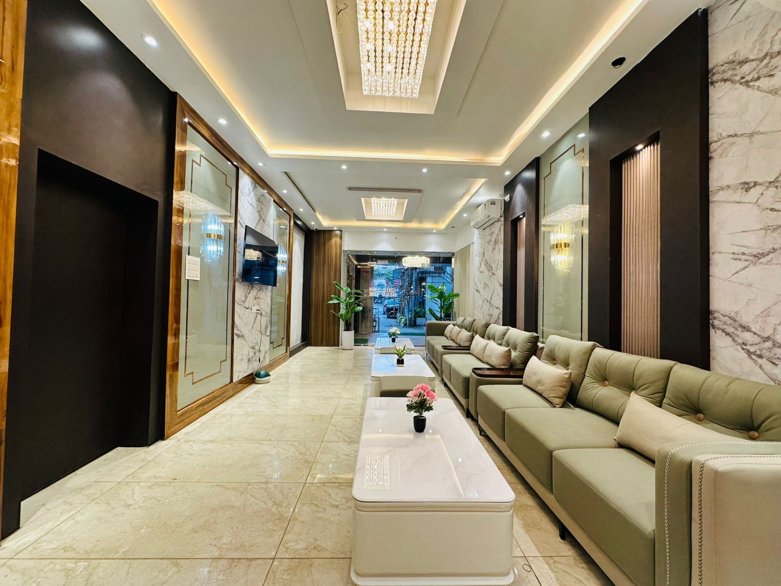A modern hotel lobby with a marble floor, a white coffee table with flowers, a leather sofa, and a chandelier.