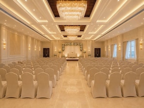 A large, well-lit hall with rows of chairs, a stage with floral decorations, and a chandelier. - HOTEL ADITYA MARINE GARDEN (Patna)