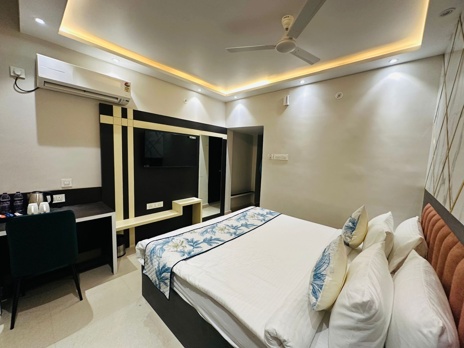 Ein Hotelzimmer mit Bett, Schreibtisch, Fernseher und Deckenventilator.