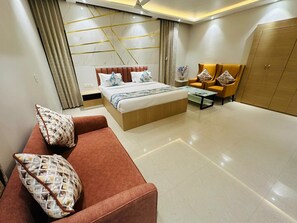 A modern bedroom with a bed, a sofa, a coffee table, and a wardrobe. - HOTEL ADITYA MARINE GARDEN (Patna)