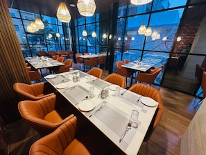 A restaurant with tables set for dining, large windows, and hanging light fixtures. - HOTEL ADITYA MARINE GARDEN (Patna)