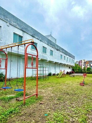 A playground with swings and slides, a grassy area, and a building with multiple windows in the background.