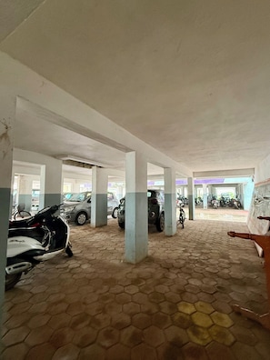 A parking area with hexagonal tiles, concrete pillars, and parked vehicles including cars and a motorcycle.