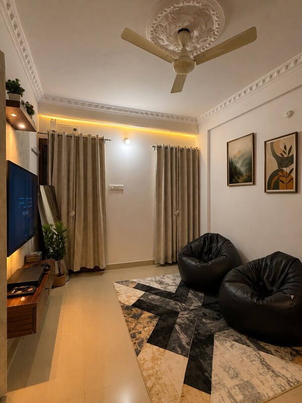 Un salon avec un ventilateur de plafond, deux fauteuils poire, un téléviseur à écran plat et un tapis à motifs.