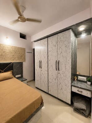A bedroom with a bed, wardrobe, vanity, and ceiling fan.