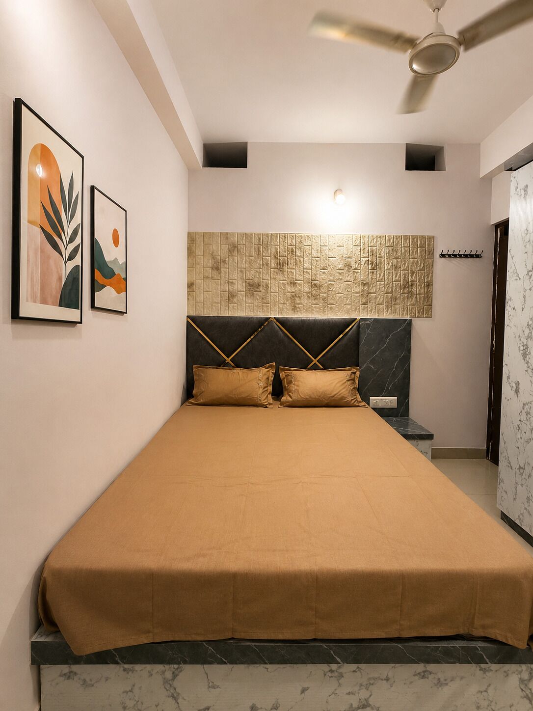 Ein Schlafzimmer mit einem Bett, einem Deckenventilator, einer Wandleuchte und zwei gerahmten Kunstwerken.