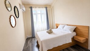 Ein Schlafzimmer mit einem Bett, einem Nachttisch, einem Spiegel und einem Fenster mit Vorhängen.