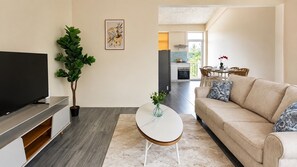 A modern living room with a flat-screen TV, a coffee table, a sofa, and a dining area in the background. - Tropical Escape: Spacious 3-Bedroom Apartment in Blue Bay (Mahebourg)