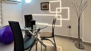 Un'area pranzo moderna con tavolo in vetro, sedie e un'installazione luminosa geometrica sulla parete.