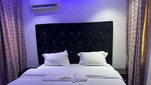 Un letto rifatto con lenzuola e cuscini bianchi, una testata imbottita e un asciugamano disposto sul letto.