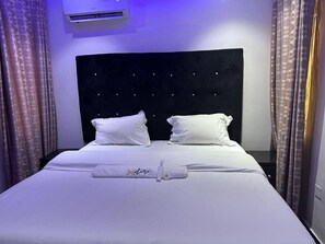 Ein ordentlich bezogenes Bett mit weißen Leinen und Kissen, ein Kopfteil mit gepolstertem Design und ein Handtuch auf dem Bett.