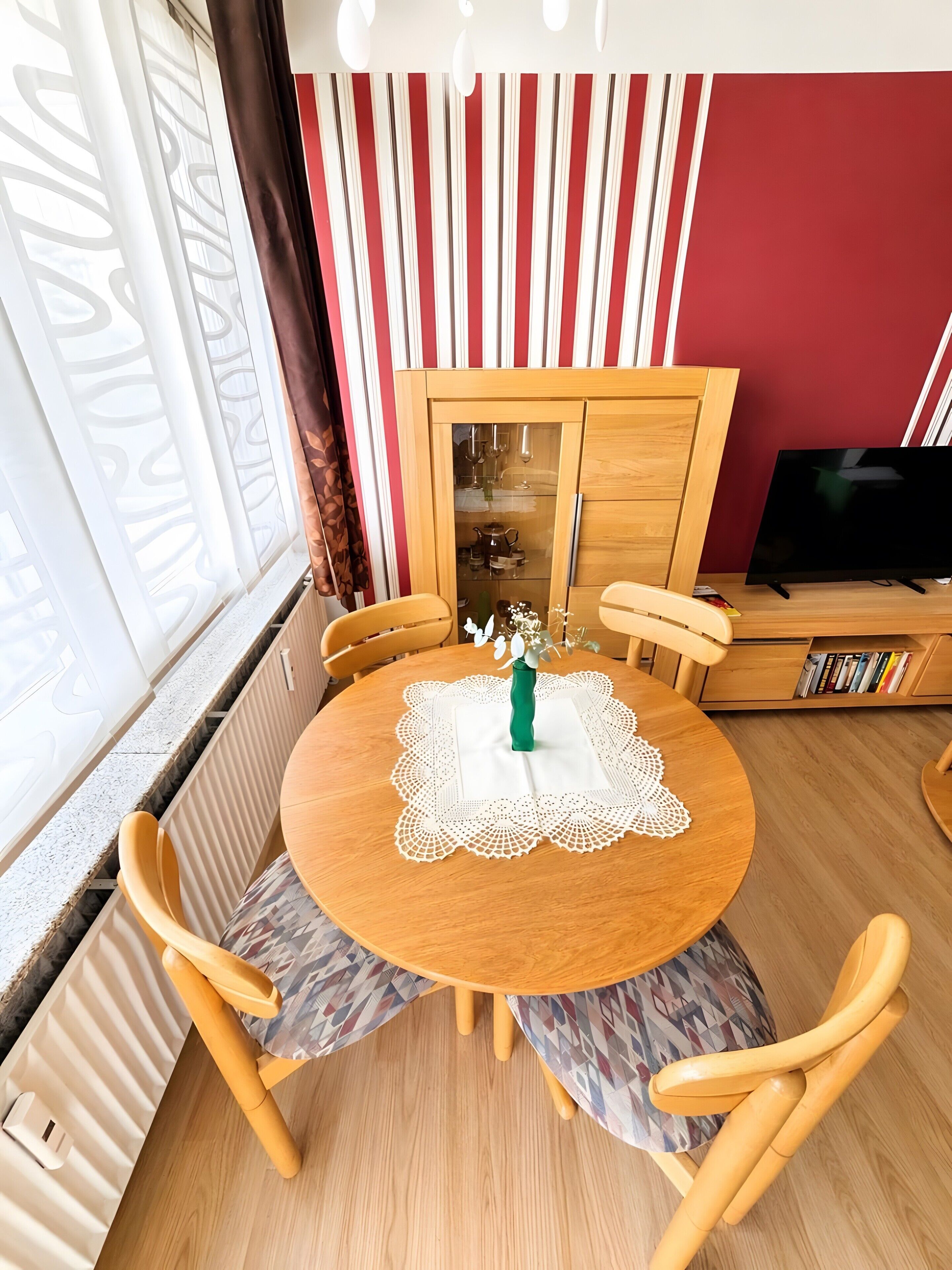 A dining area with a round wooden table, four chairs, a vase with flowers, and a cabinet with glass doors.