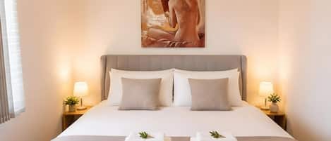 A hotel room with a large bed, two bedside lamps, a painting on the wall, and a window with curtains.